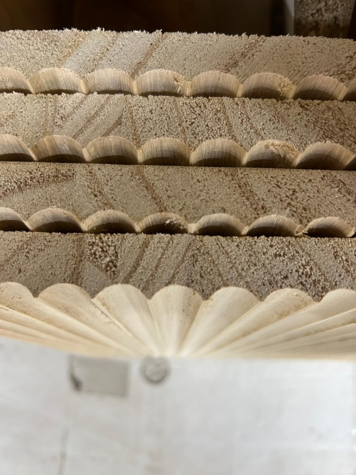 Primo piano di una parete o superficie decorativa beige, smerlata e a forma di ventaglio, con una texture particolare.