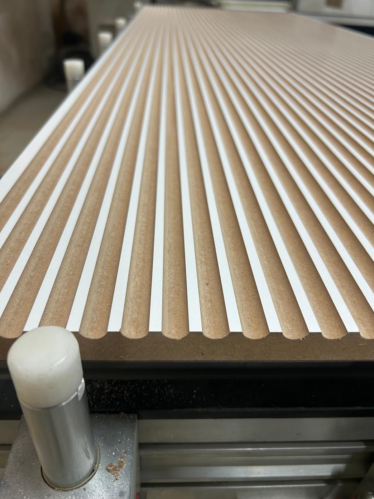 Pannello a doghe di legno su una macchina, visto di profilo con una guida metallica davanti.