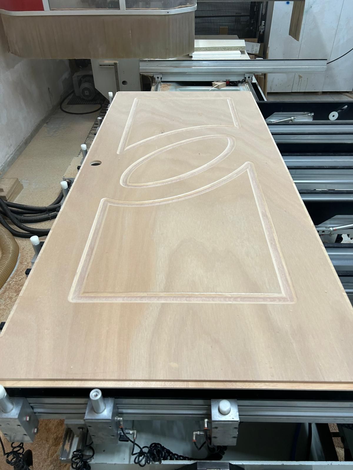 Una macchina a controllo numerico (CNC) intaglia un pannello con un grande disegno a forma di foglia in un'officina.