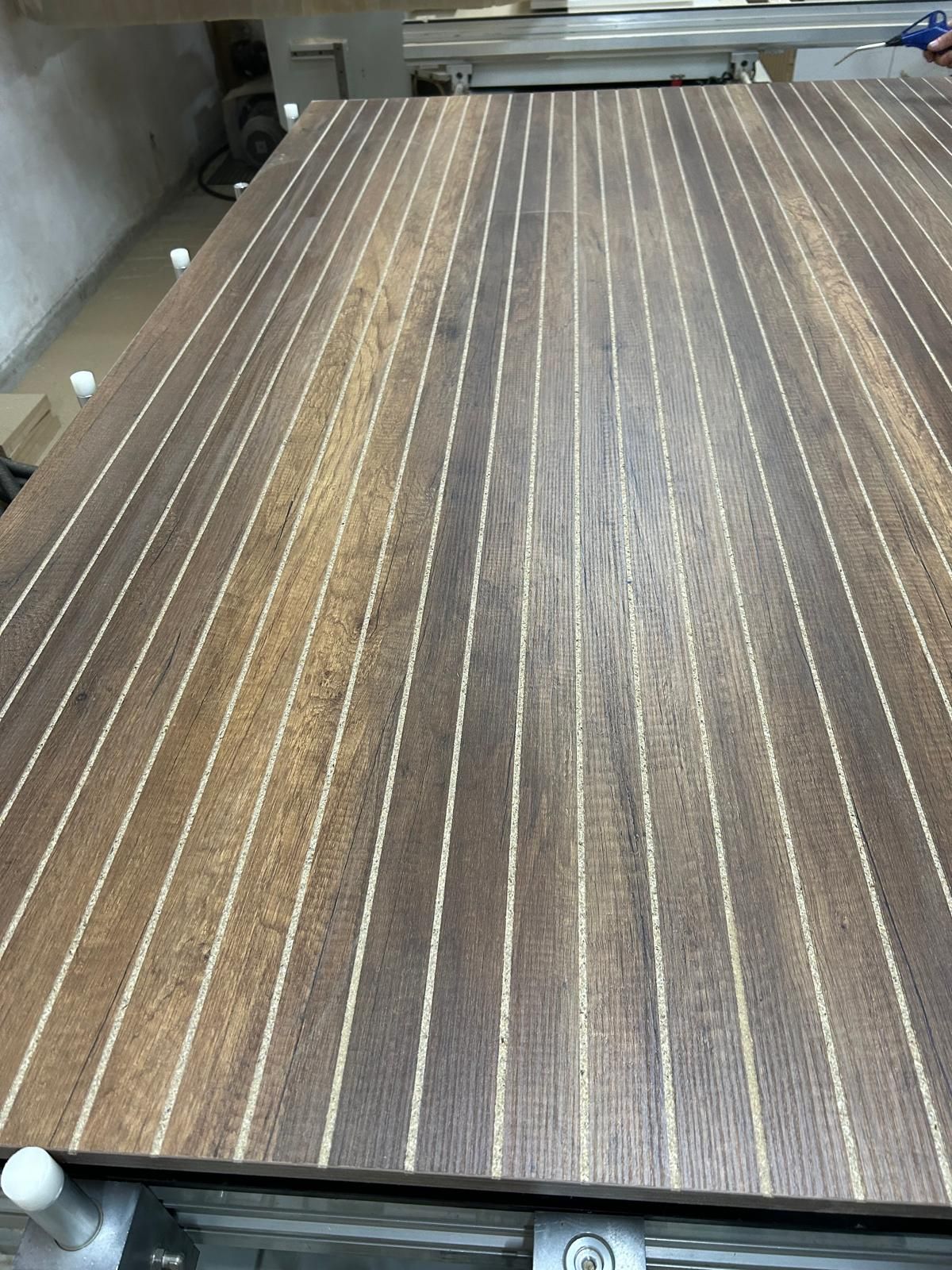 Piano di un tavolo in legno con venature a righe e paracolpi angolari bianchi in un ambiente da officina.