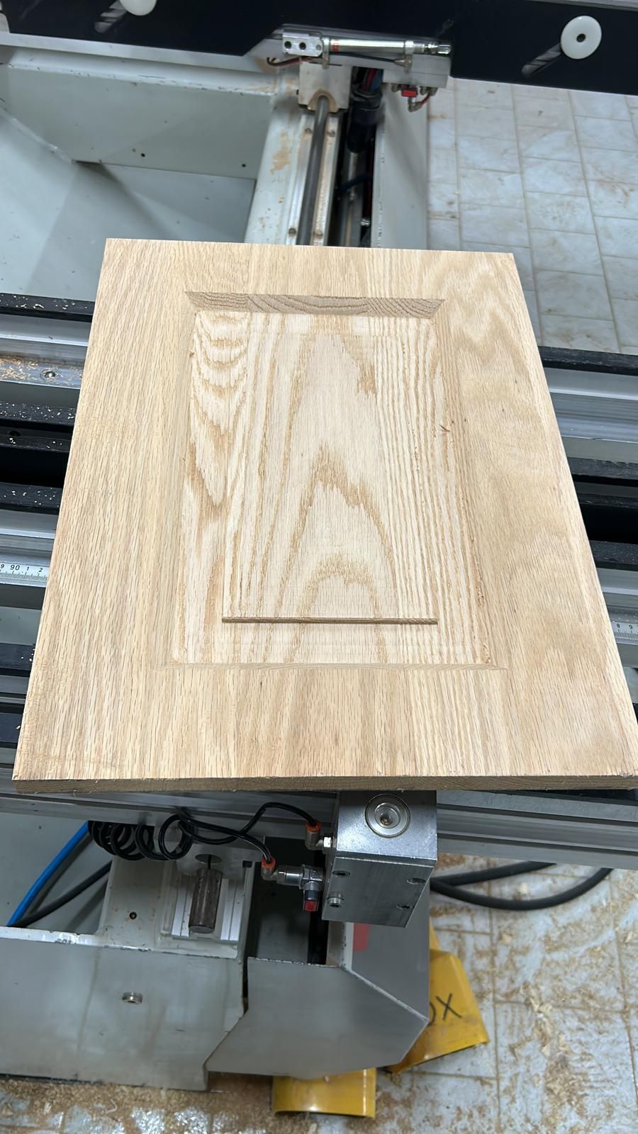 Tavola di legno sul banco di una macchina a controllo numerico, vista dall'alto.