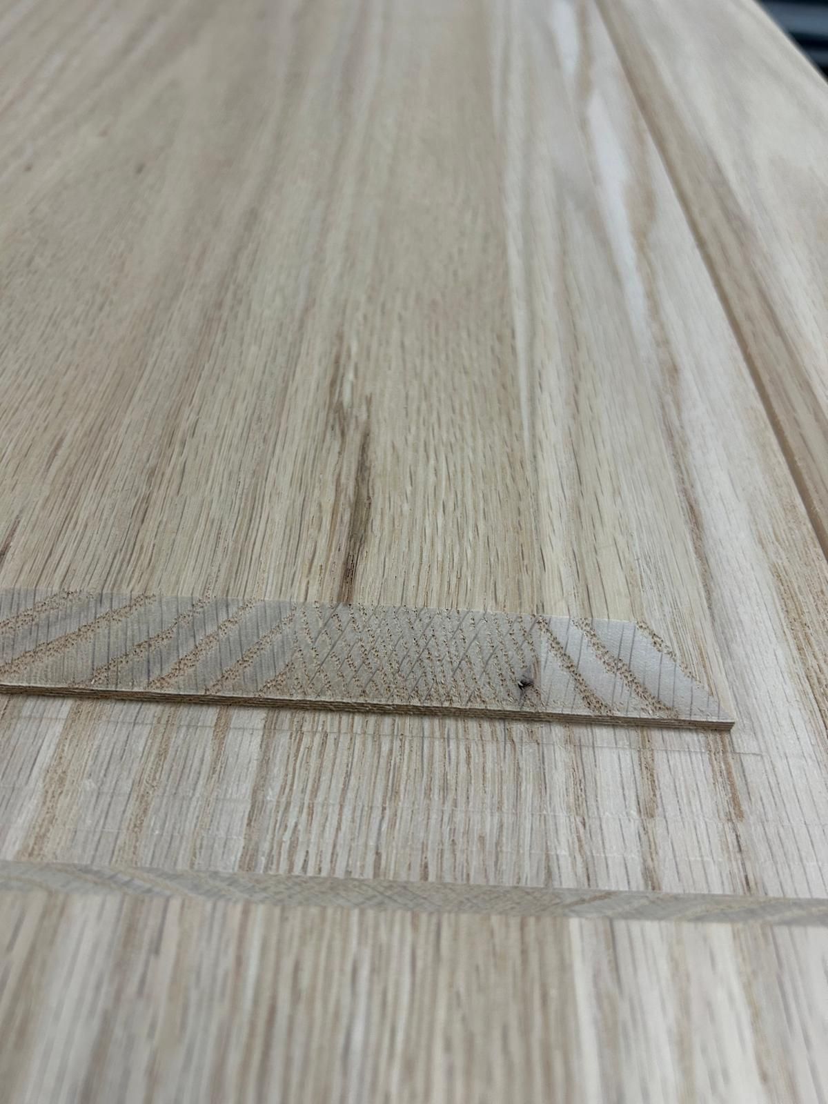 Primo piano di un pavimento in legno chiaro con venature a vista e una giunzione scura vicino al bordo inferiore.