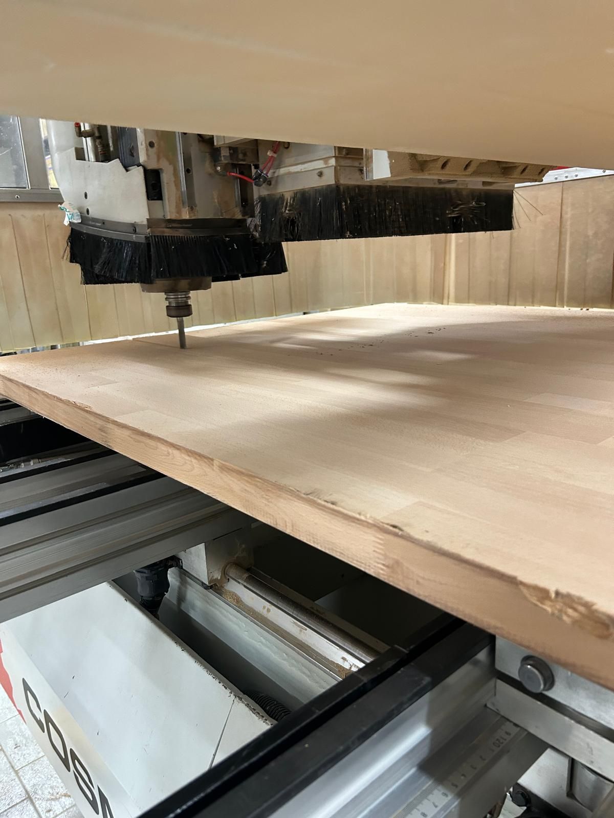 Una fresatrice CNC taglia un grande pannello di legno su un banco da lavoro in un'officina.