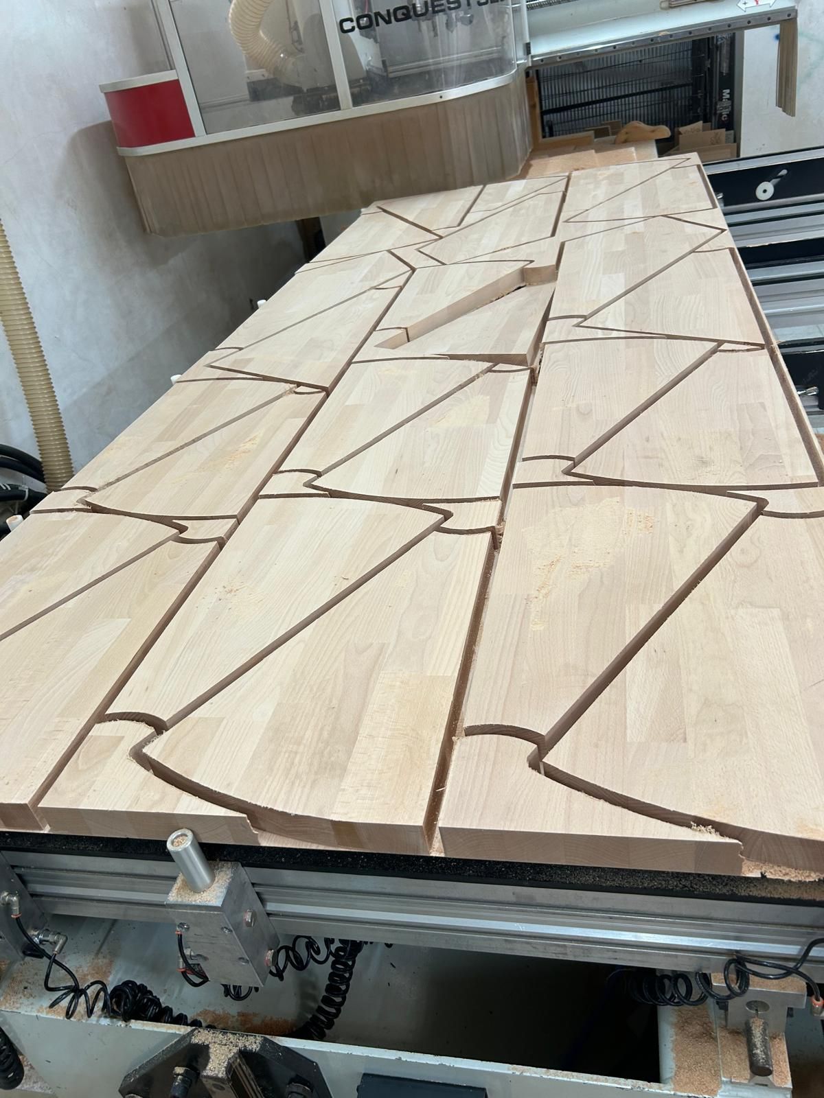 Pannello con motivo effetto legno su un tavolo di una macchina a controllo numerico (CNC) con linee di taglio triangolari e giunture intarsiate marroni.