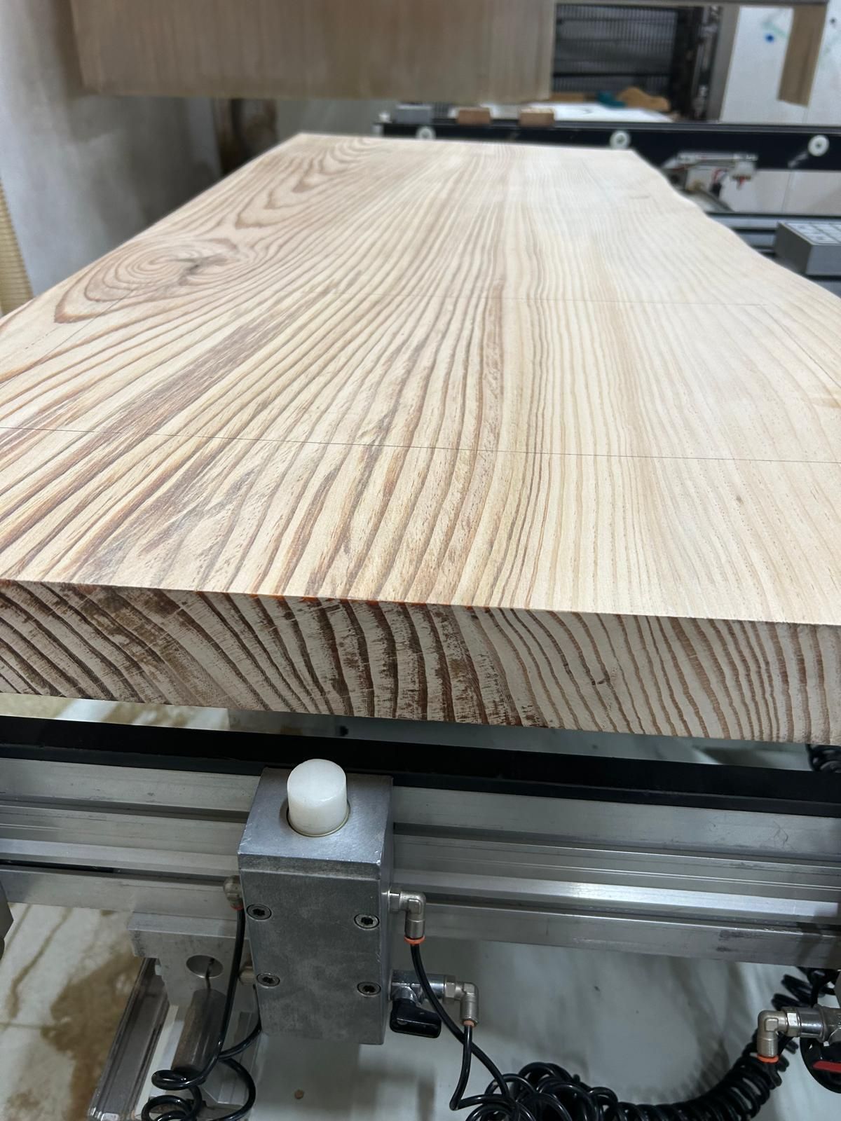 Una tavola di legno su un nastro trasportatore in un'officina, vista frontalmente.