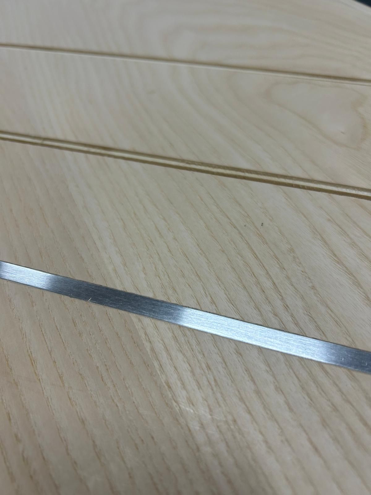 Primo piano di un pavimento in legno chiaro con una sottile striscia di metallo argentato che lo attraversa.