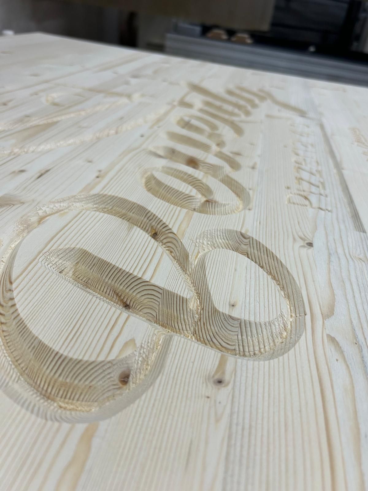 Logo inciso su una superficie in legno di pino chiaro, visto da un'angolazione diversa.