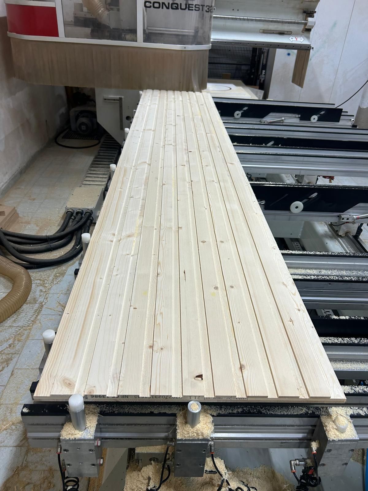 Listelli di legno impilati sul banco di una macchina CNC in un'officina