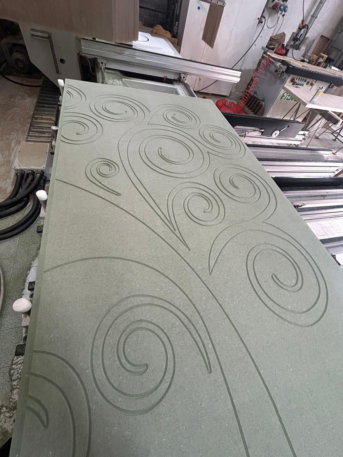 Pannello decorativo grigio con motivi a spirale e a vite in un ambiente di officina o fabbrica.