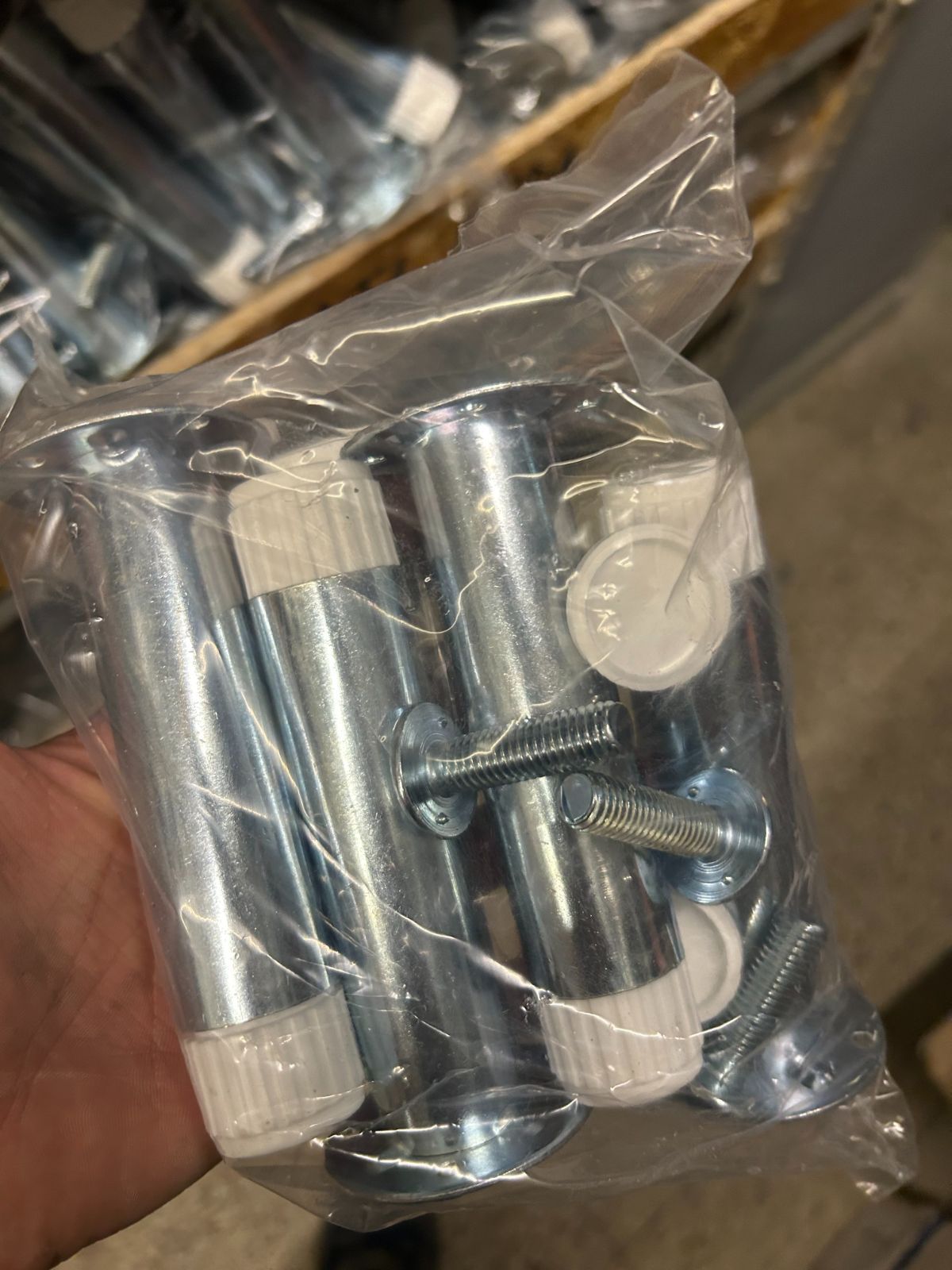 Una mano che regge un sacchetto di plastica trasparente contenente bulloni e dadi in metallo argentato.