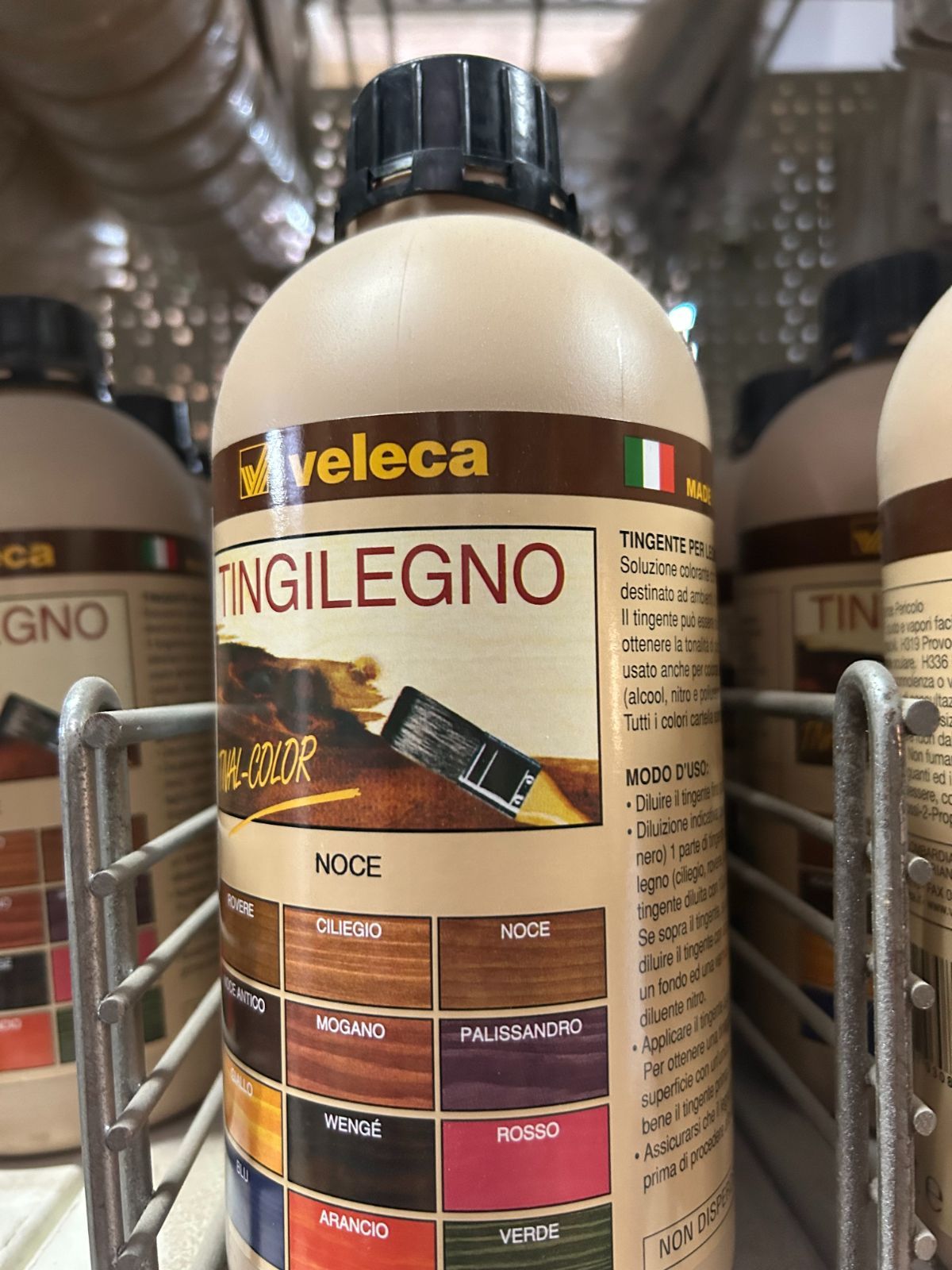 Bottiglie di mordente per legno su uno scaffale di un negozio, con una bottiglia con etichetta beige e nera al centro in primo piano.
