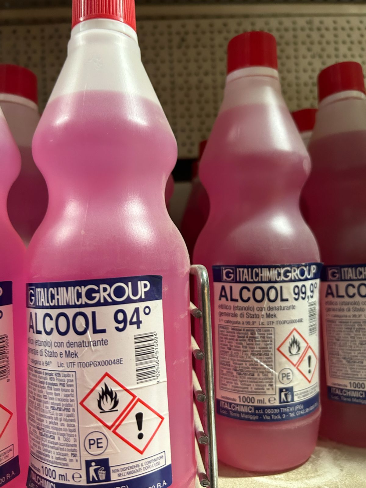 Bottiglie rosa di alcol a 94° con tappi rossi su uno scaffale di un negozio.