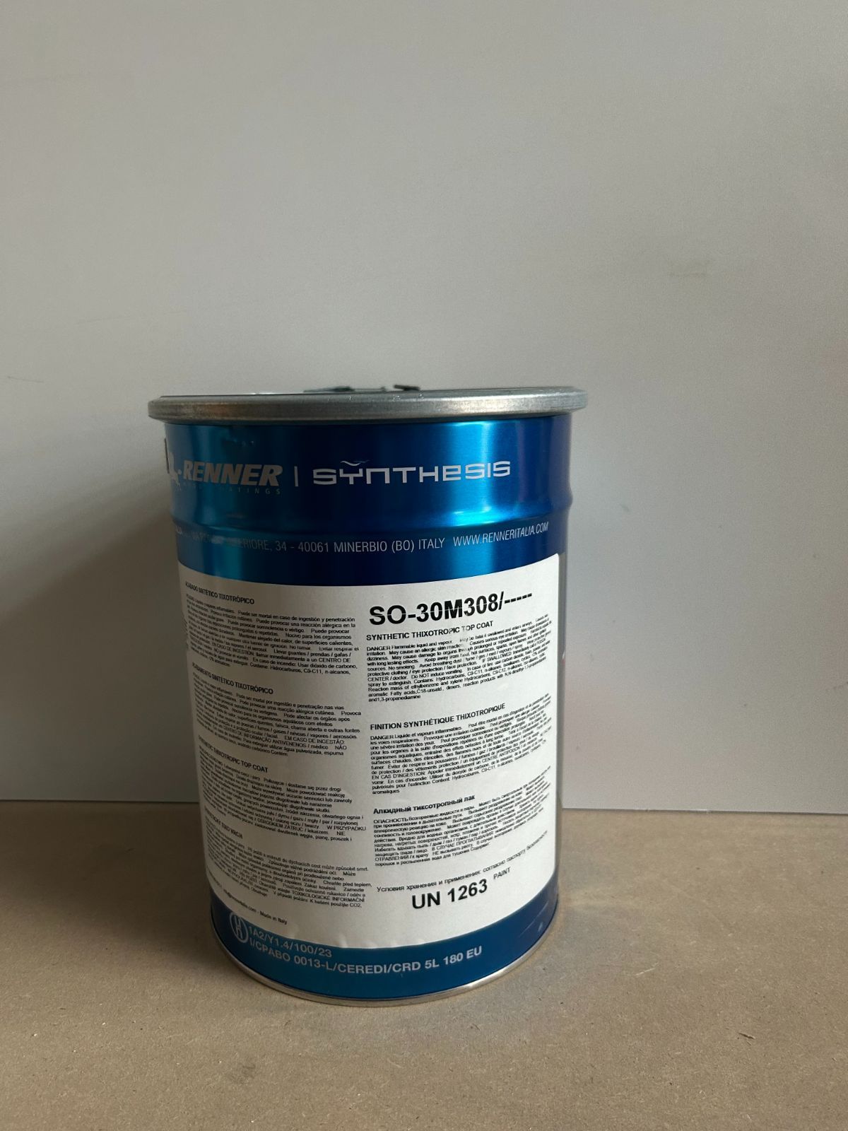 Contenitore metallico blu e bianco con etichetta, appoggiato su un tavolo contro una parete spoglia.