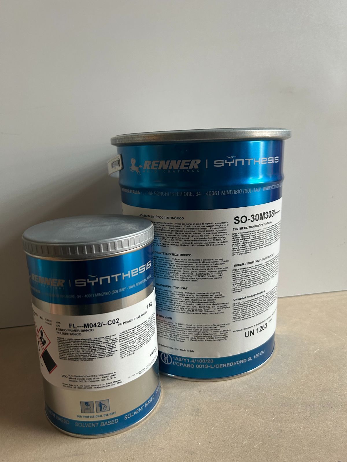 Due lattine di detersivo Reemer blu e bianche su una superficie piana contro una parete bianca.