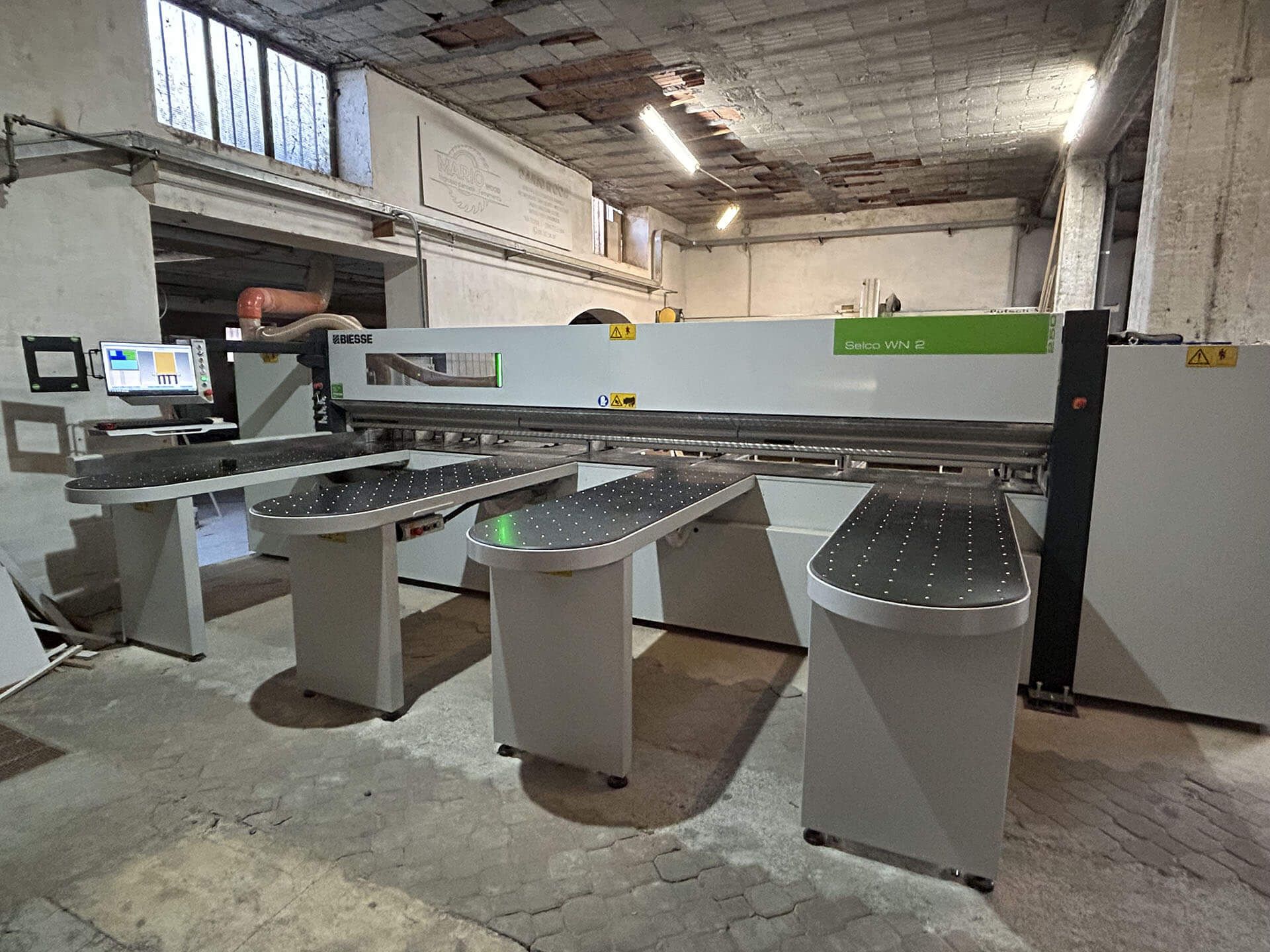 Officina industriale con una grande macchina CNC grigia su tavoli da lavoro in metallo in un locale industriale fatiscente.