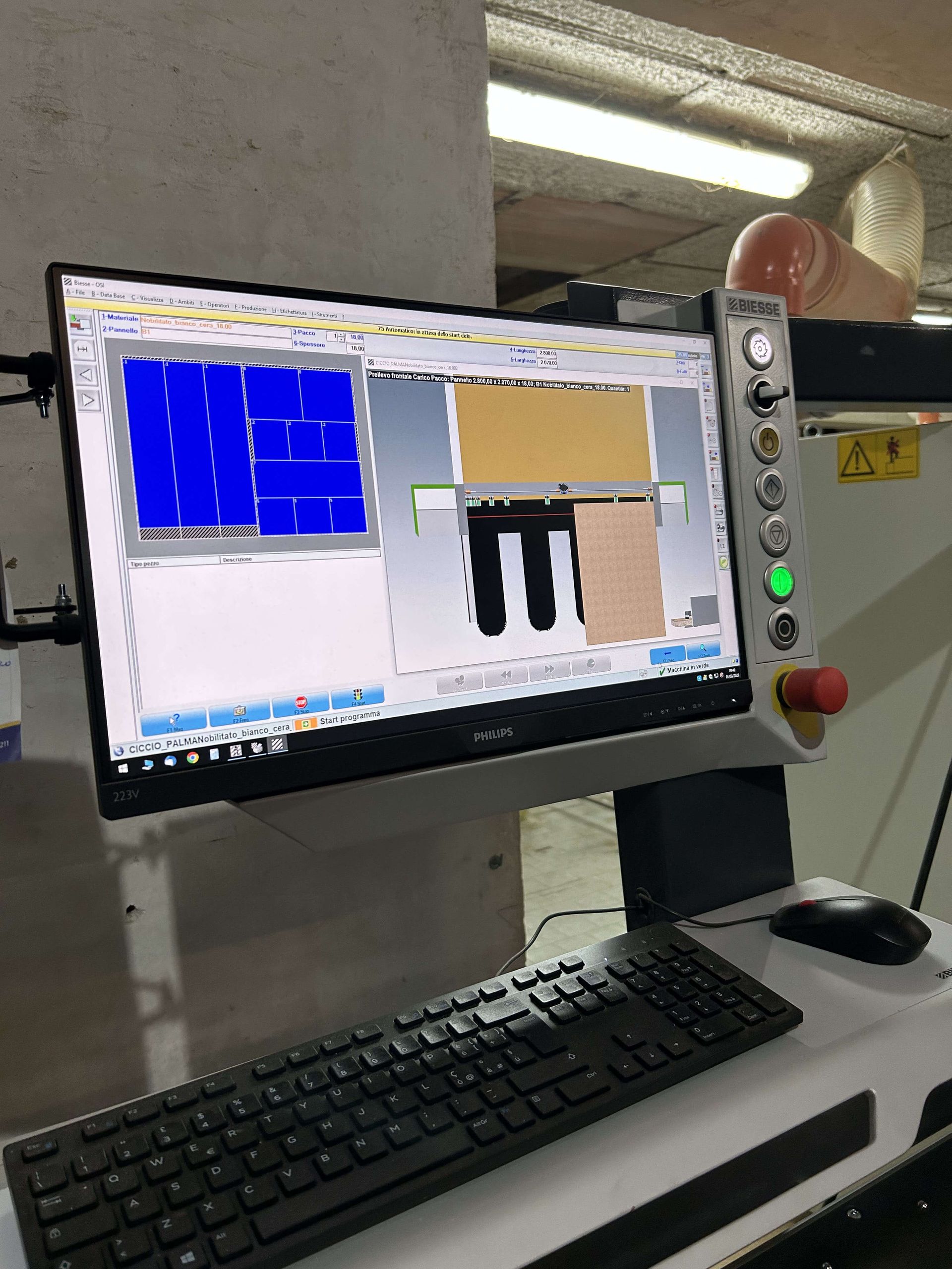 Postazione di lavoro industriale con monitor che visualizza grafici e comandi, tastiera e pulsante di arresto di emergenza nelle vicinanze.