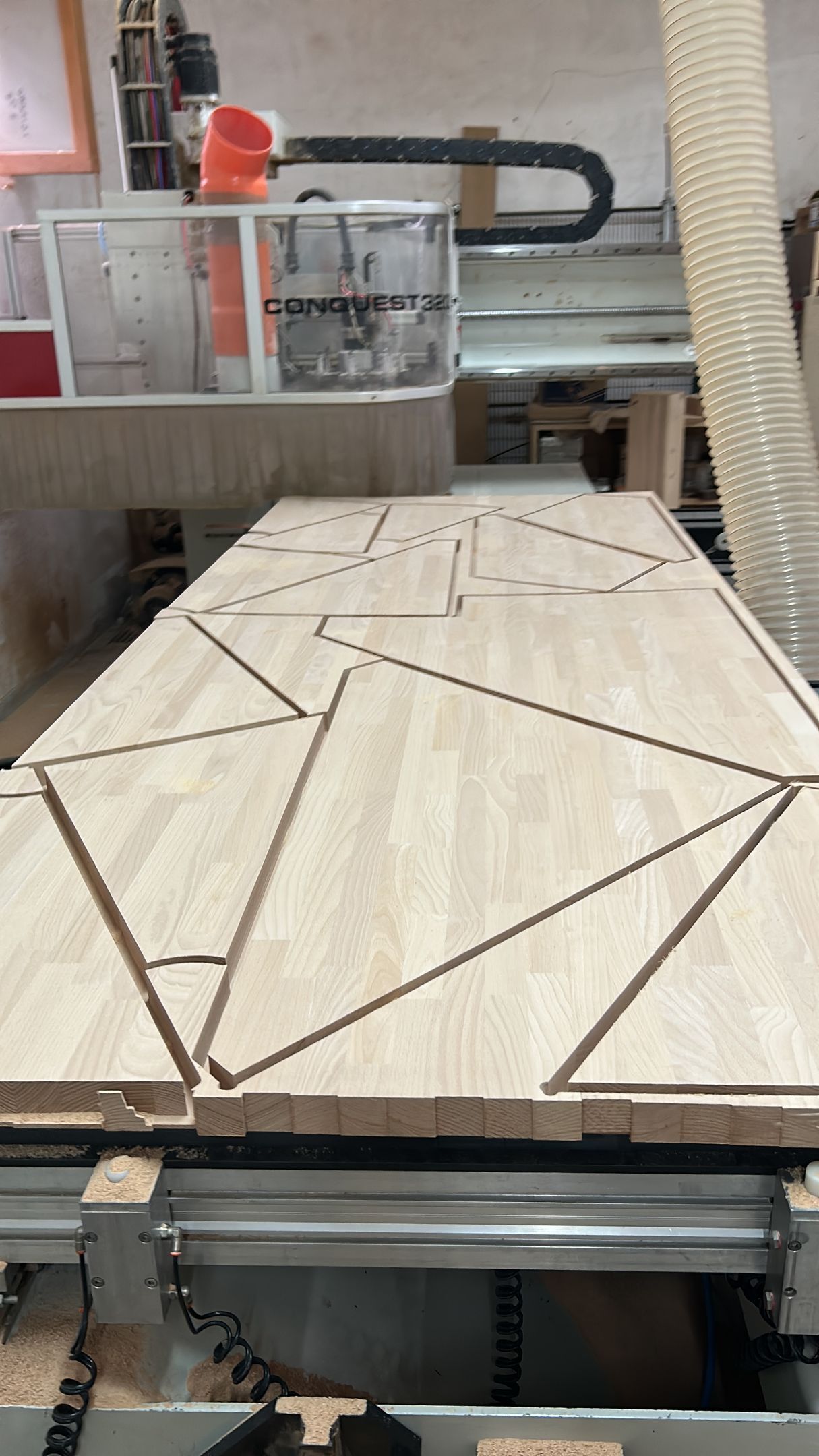 In un'officina, una fresatrice CNC taglia linee geometriche triangolari su un pannello di legno leggero.