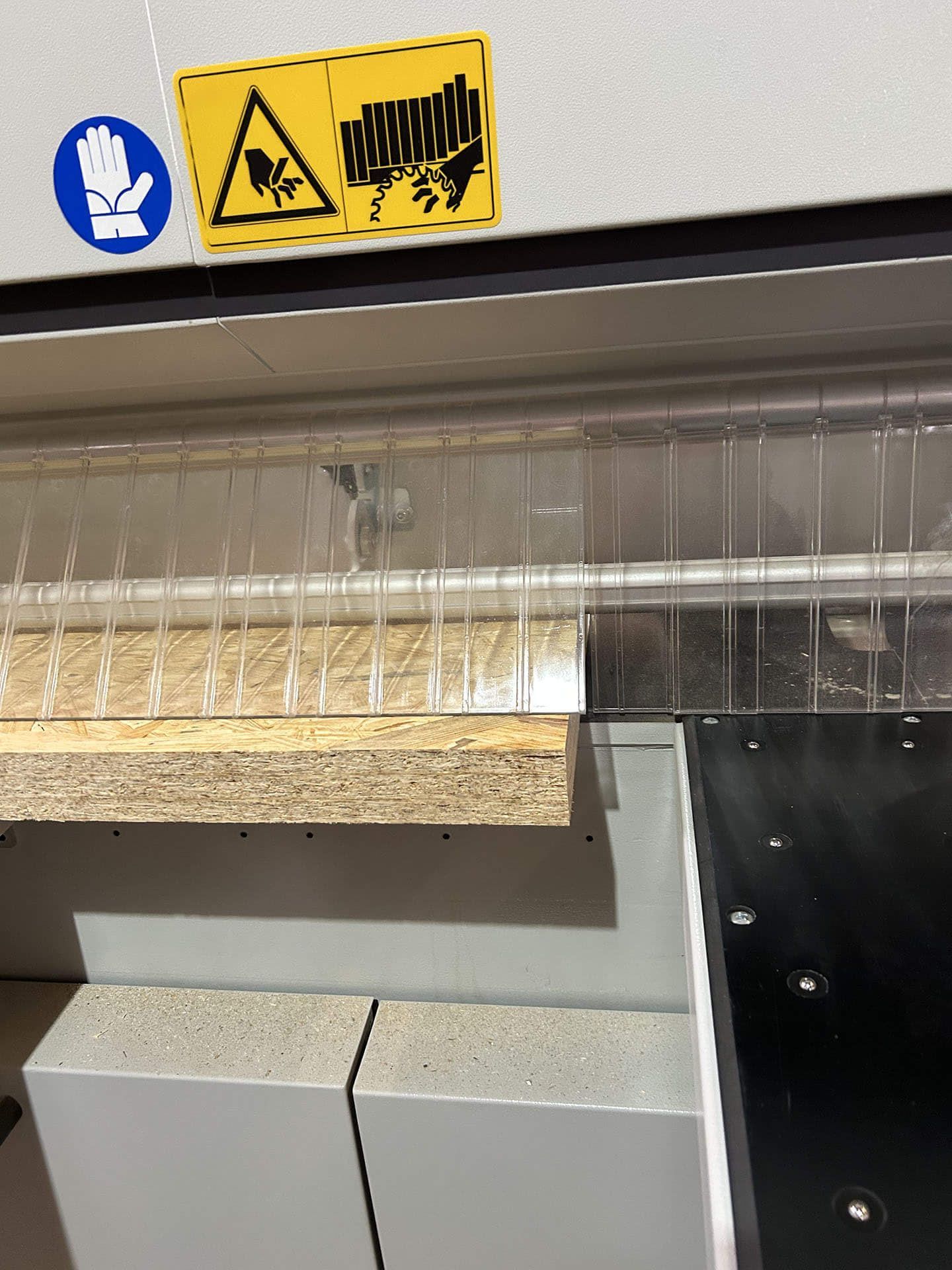 Etichette di avvertimento gialle sui macchinari industriali con tenda di plastica trasparente e pannello di legno sottostante