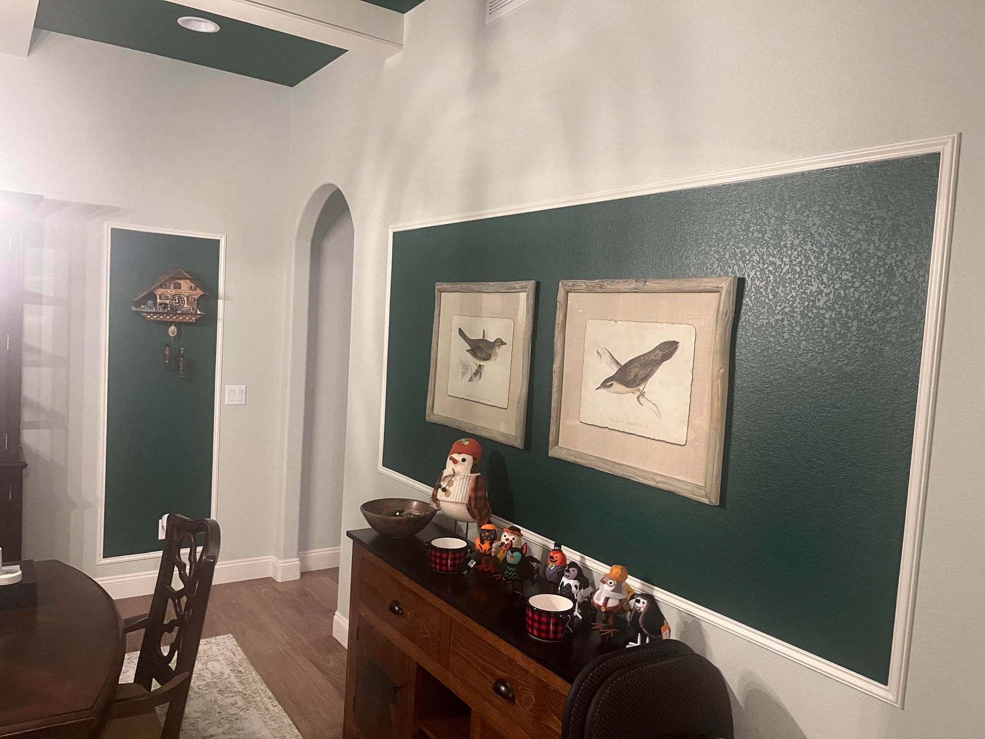 A dining room with green walls , a table , chairs , and two paintings on the wall.