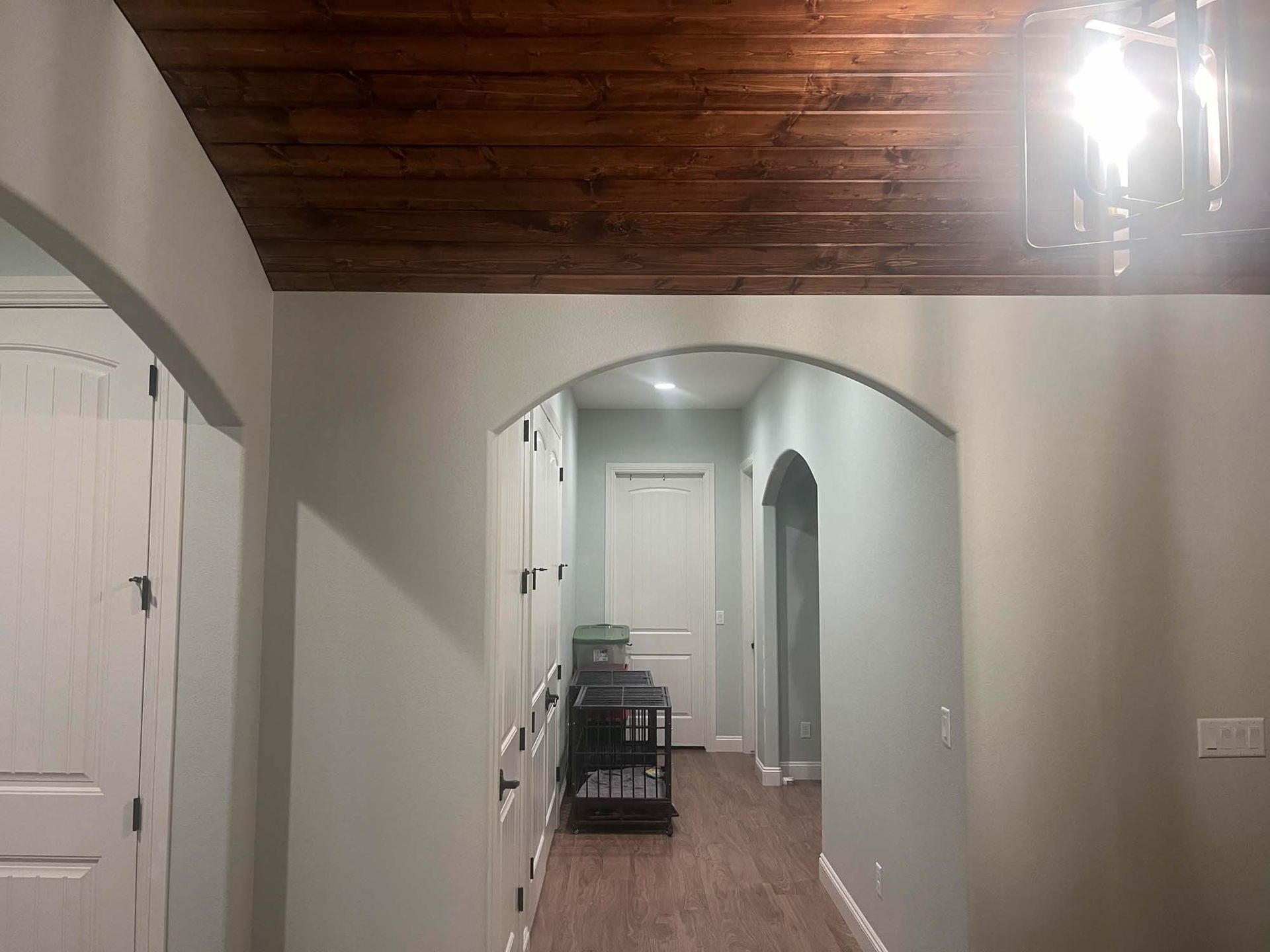 A hallway in a house with a wooden ceiling and a chandelier.