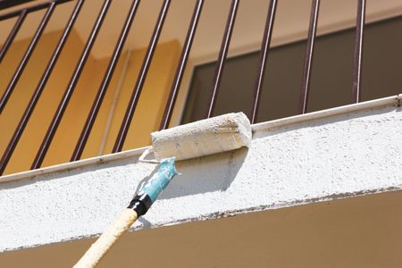 A woman is sitting on the floor painting a wall.
