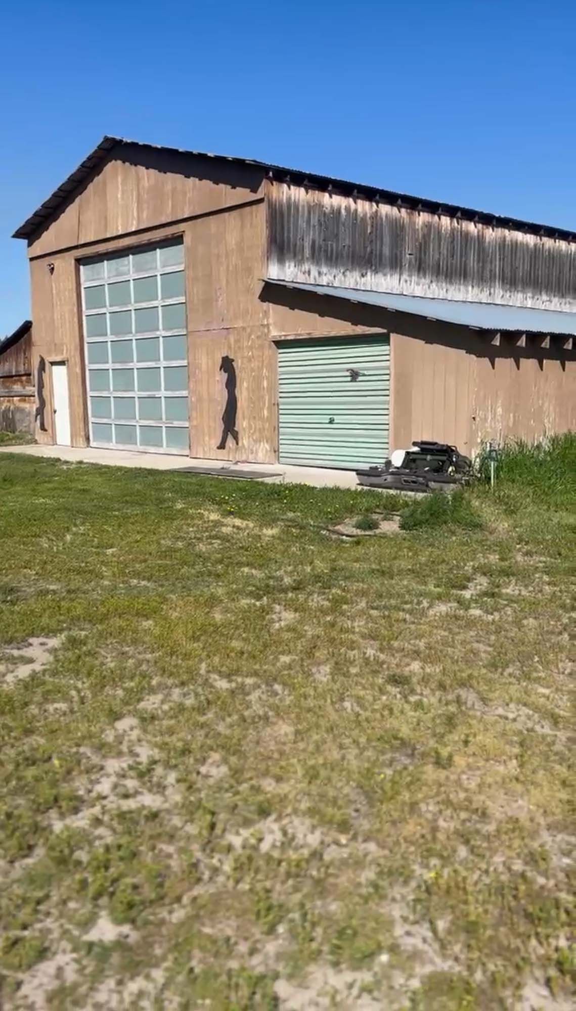 A large barn with a green garage door is sitting in the middle of a grassy field.