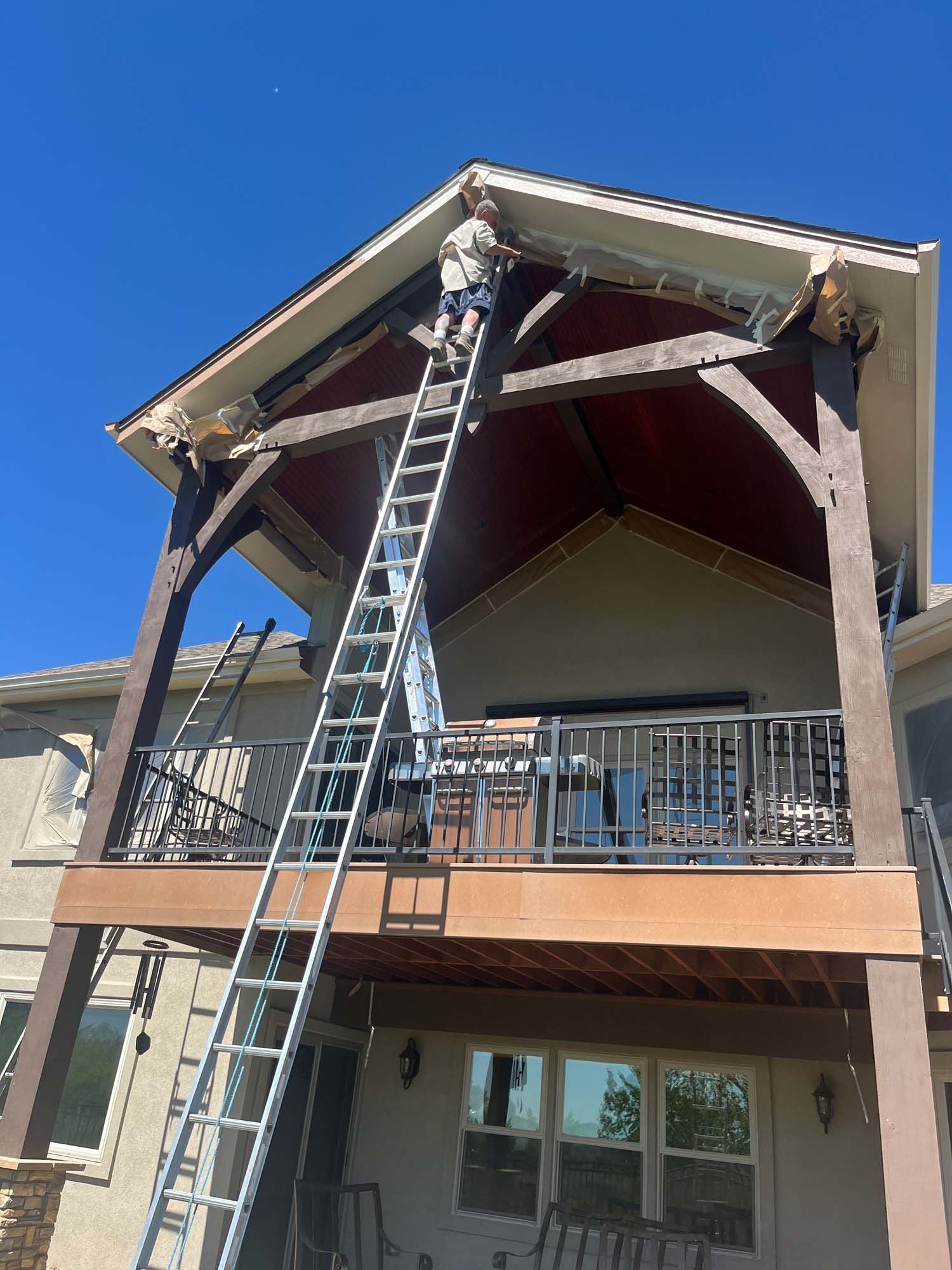 A man is standing on a ladder painting the roof of a house.