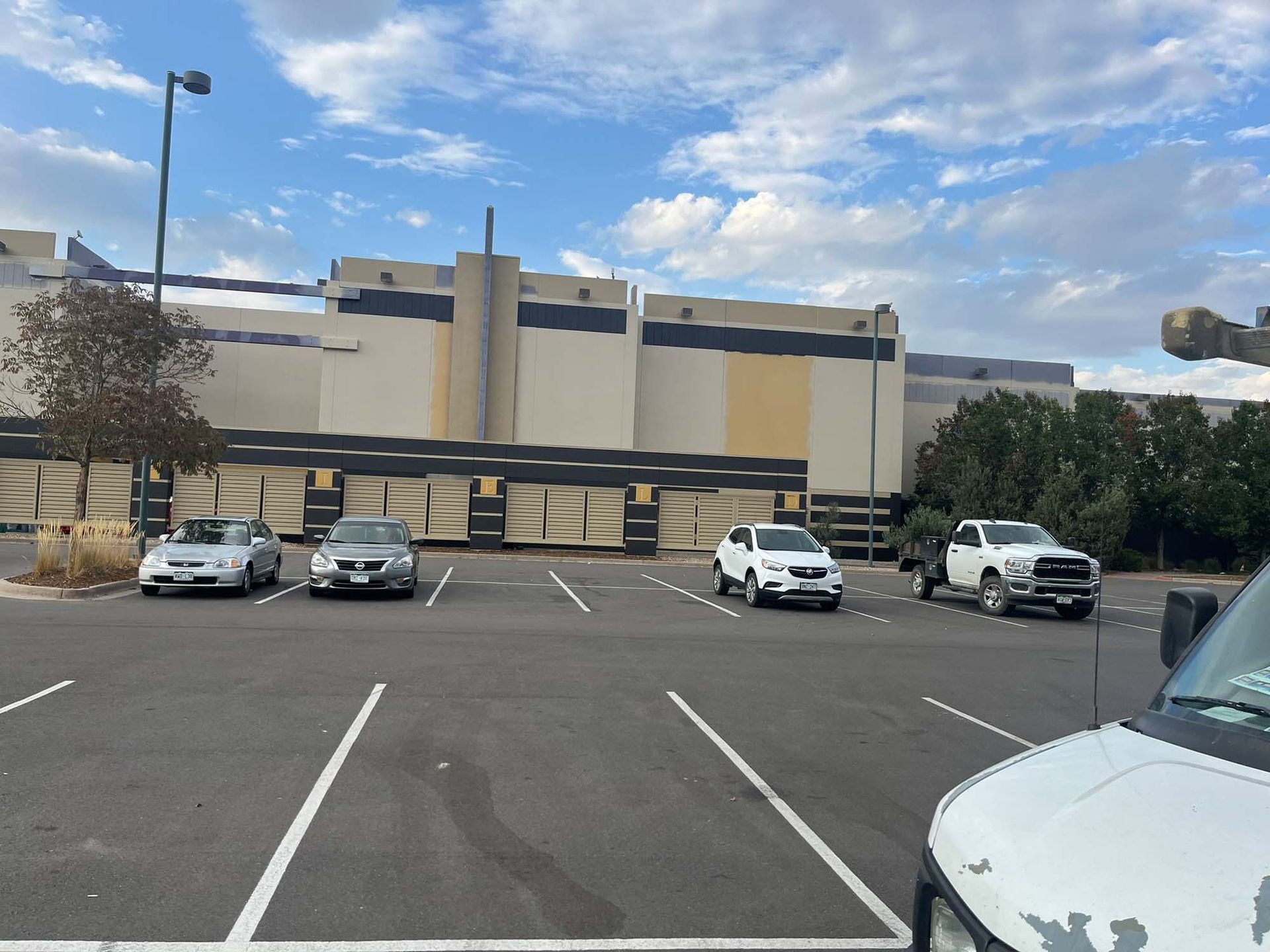 A row of cars are parked in a parking lot in front of a building.