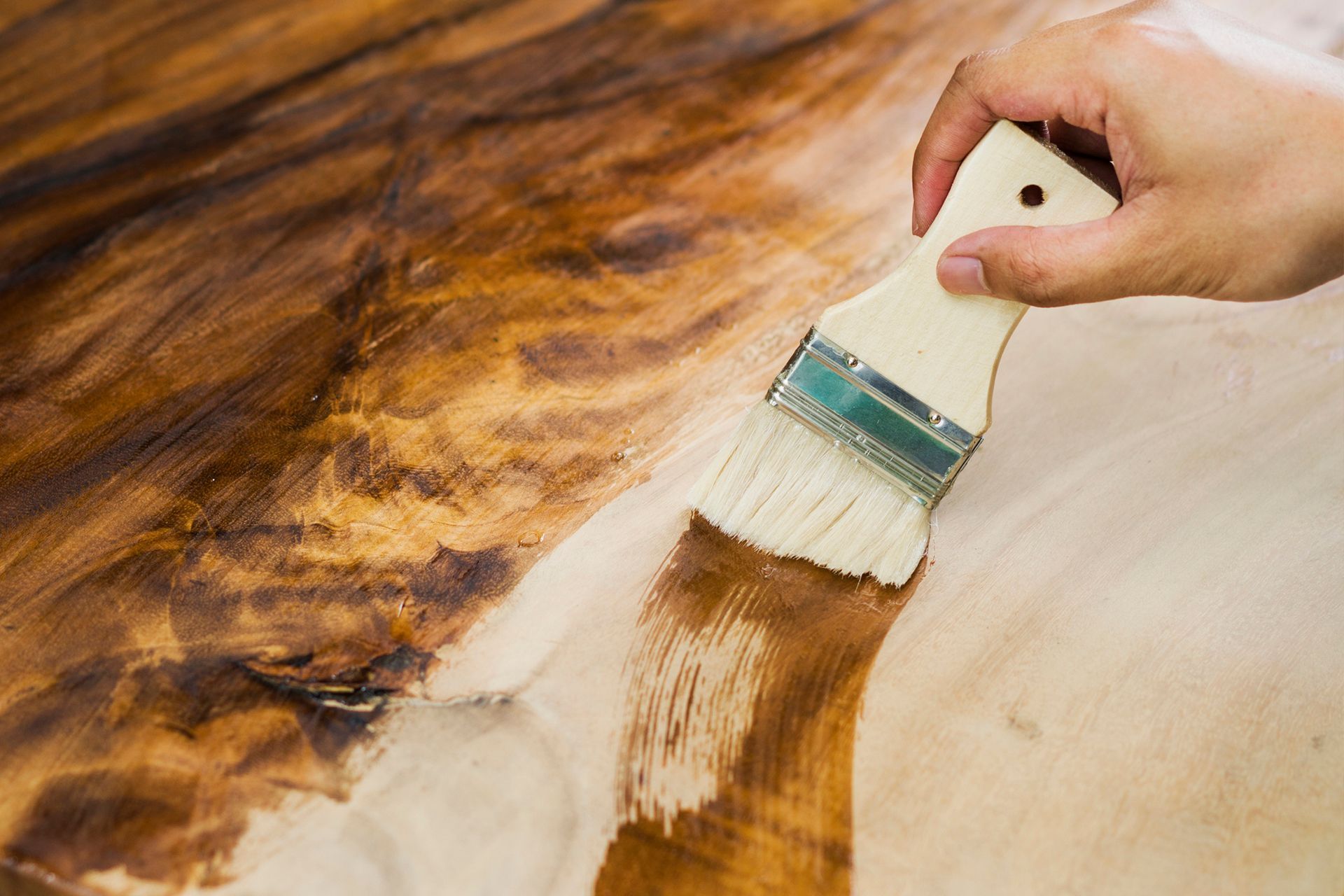 A person is painting a piece of wood with a brush. A person is painting a piece of wood with a brush.
