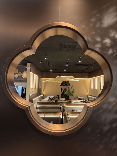 View through a clover-shaped window into a modern, warmly lit dining room with tables and hanging lights