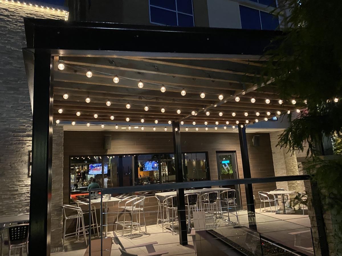 Outdoor patio with string lights, tables, and bar seating at night.