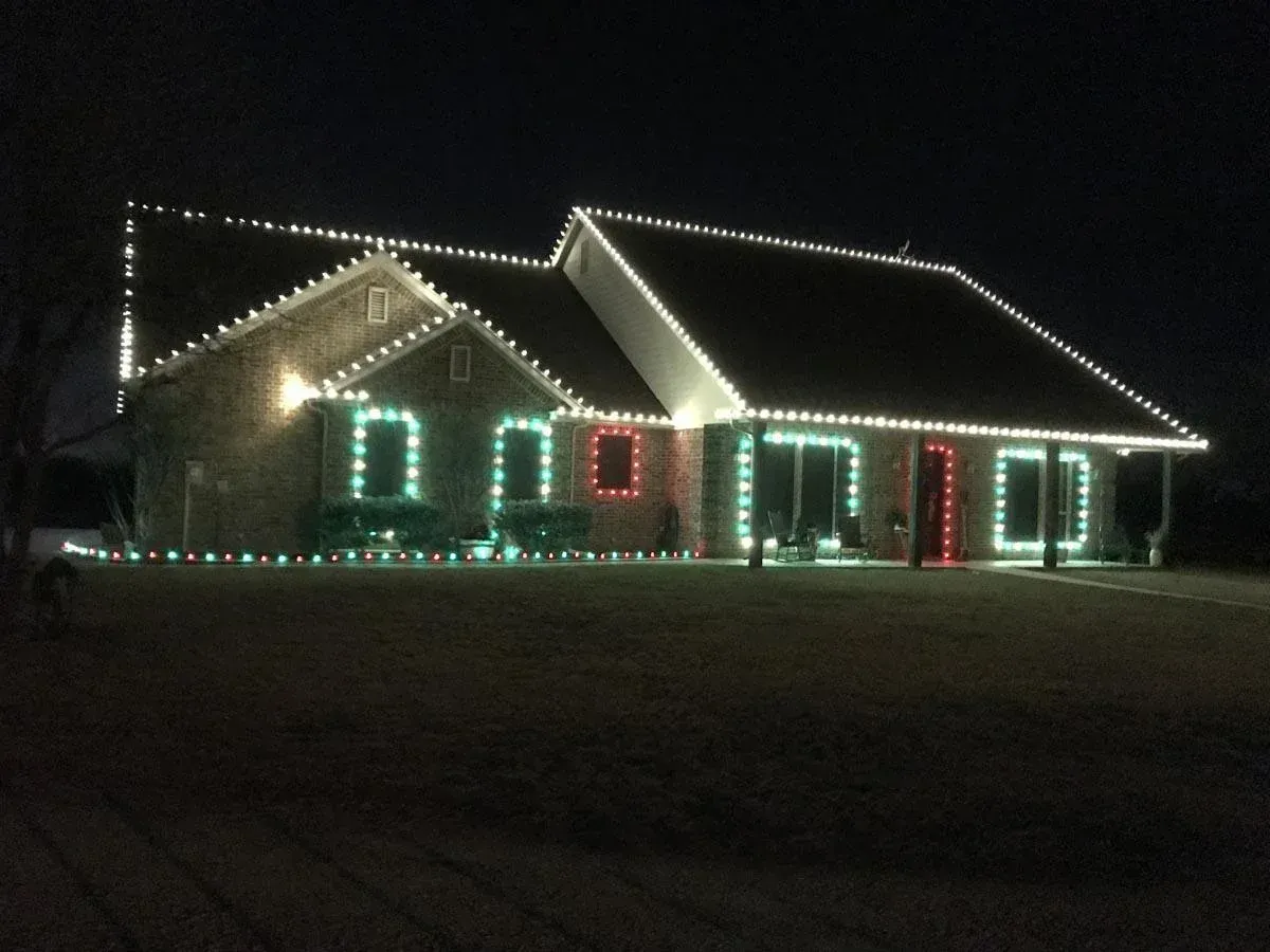 House decorated with white, green, and red Christmas lights; nighttime setting.