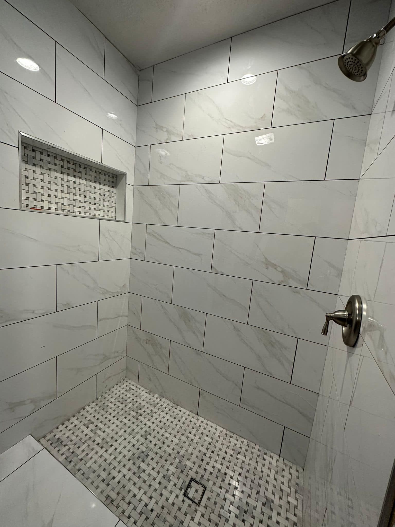 Empty tiled shower stall with a mosaic floor and wall shelf, viewed from the doorway.