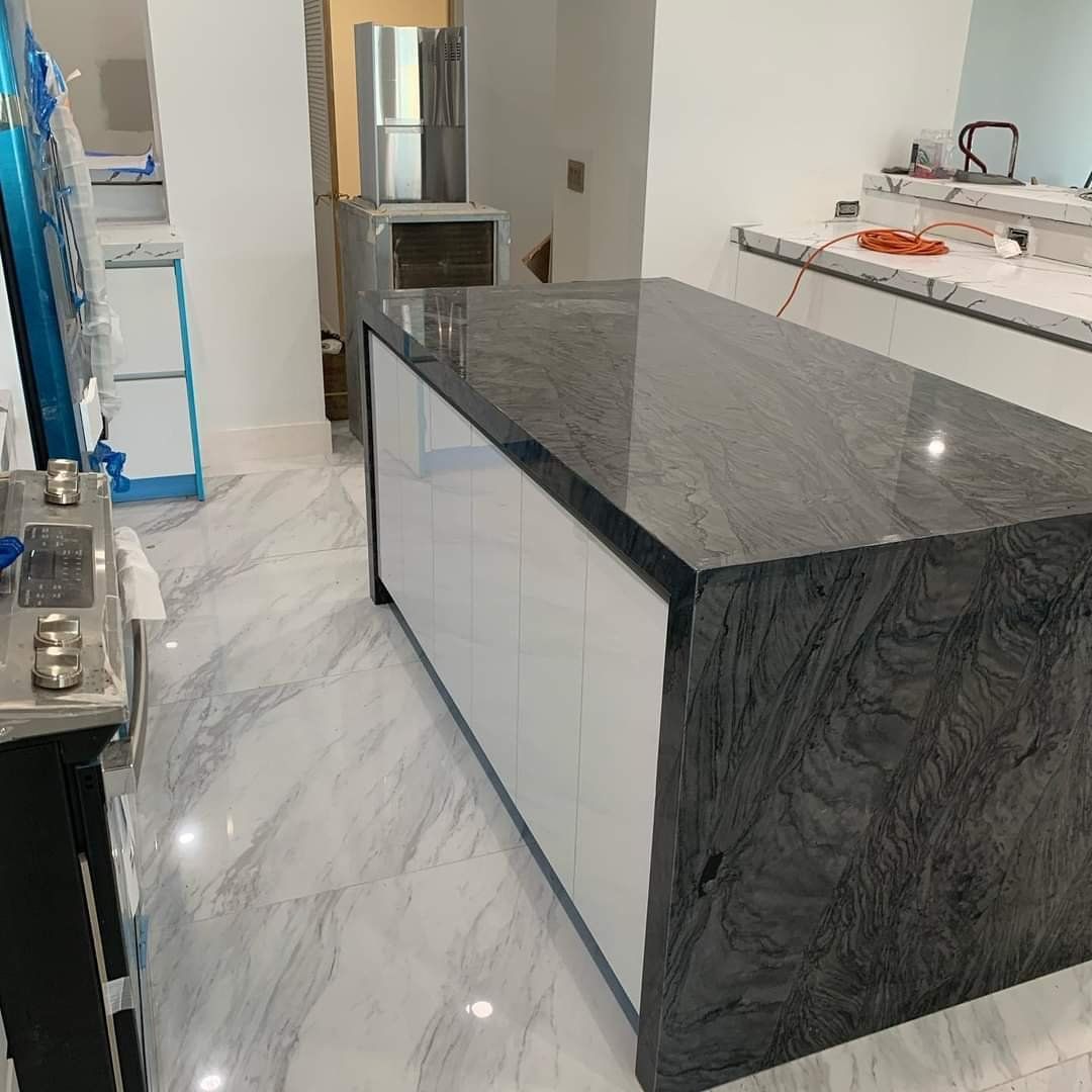 Modern kitchen with a dark granite island, white cabinets, and marble-patterned tile floor.