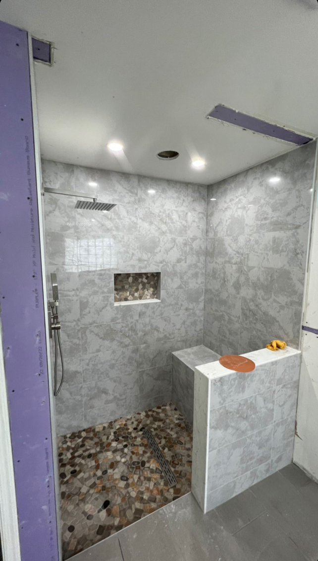 Small gray-tiled shower room with a mosaic floor, white vanity ledge, and recessed ceiling lights