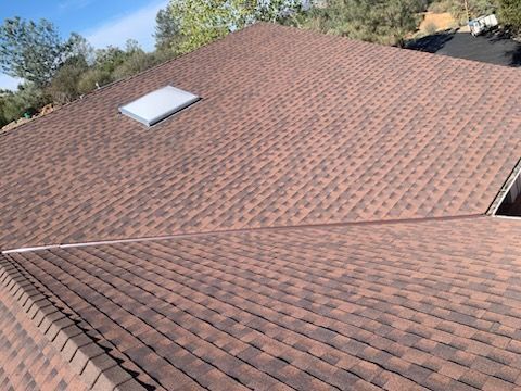 Brown shingle roof with a skylight under a clear blue sky