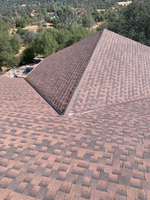 Brown shingled roof with a central peak, set against trees and hills in the background