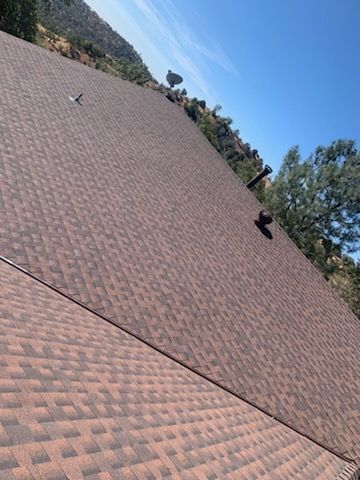 Steep shingled rooftop with two roof vents against a blue sky and trees