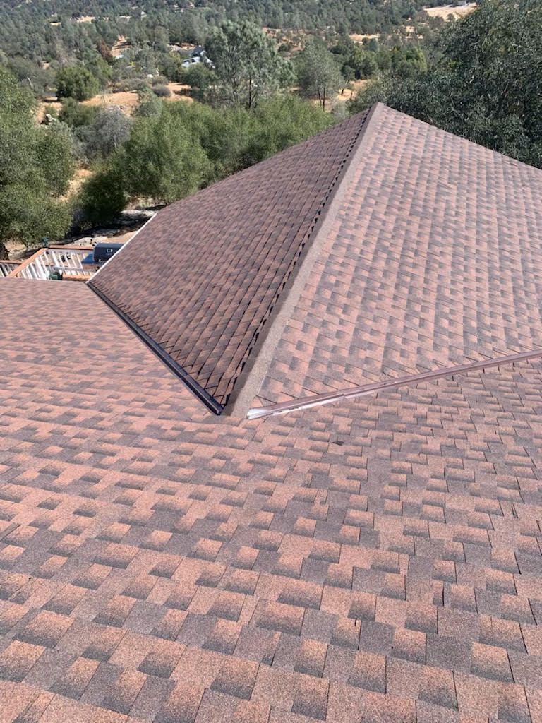 Brown shingle roof with a ridge peak, overlooking trees and hills in the background