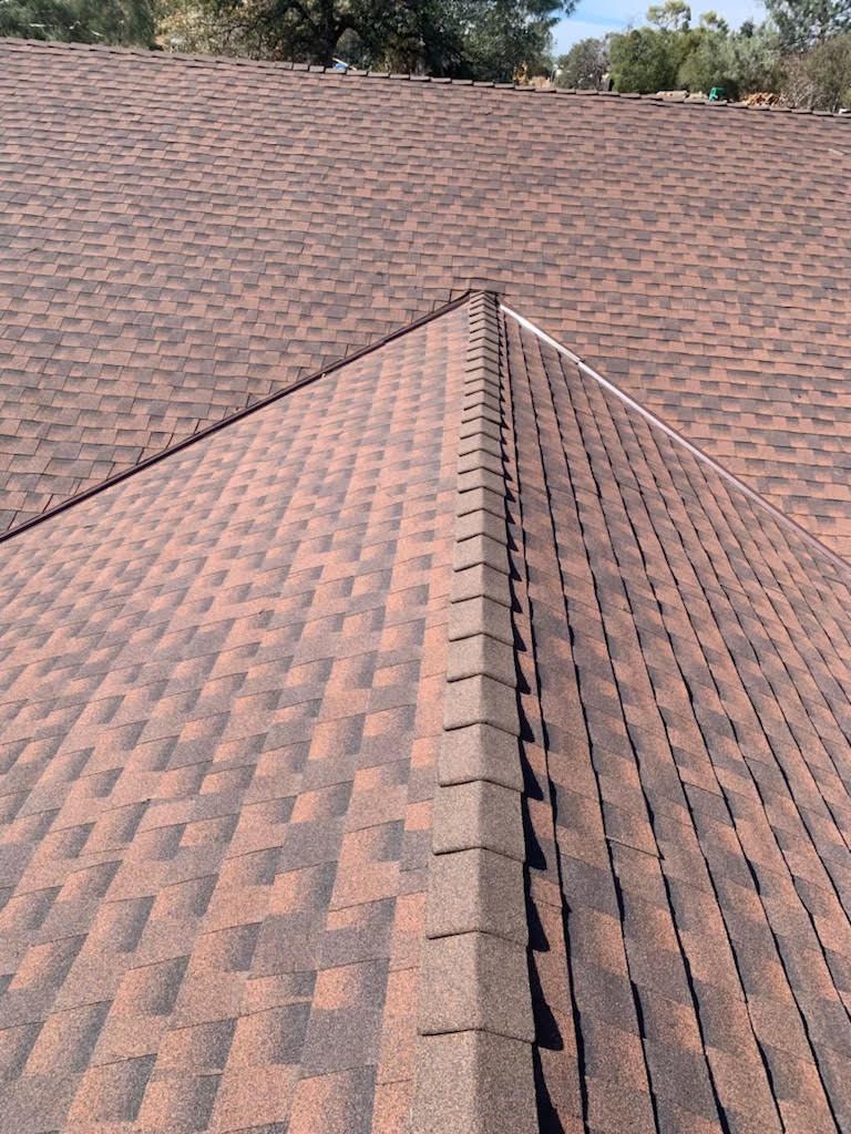 Rooftop ridge with brown shingles under a clear sky, viewed from above
