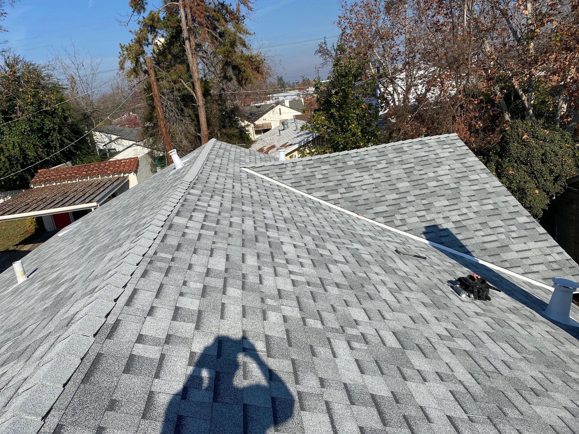 Gray shingled roof with rooftop shadows, viewed from the ridge in a suburban neighborhood