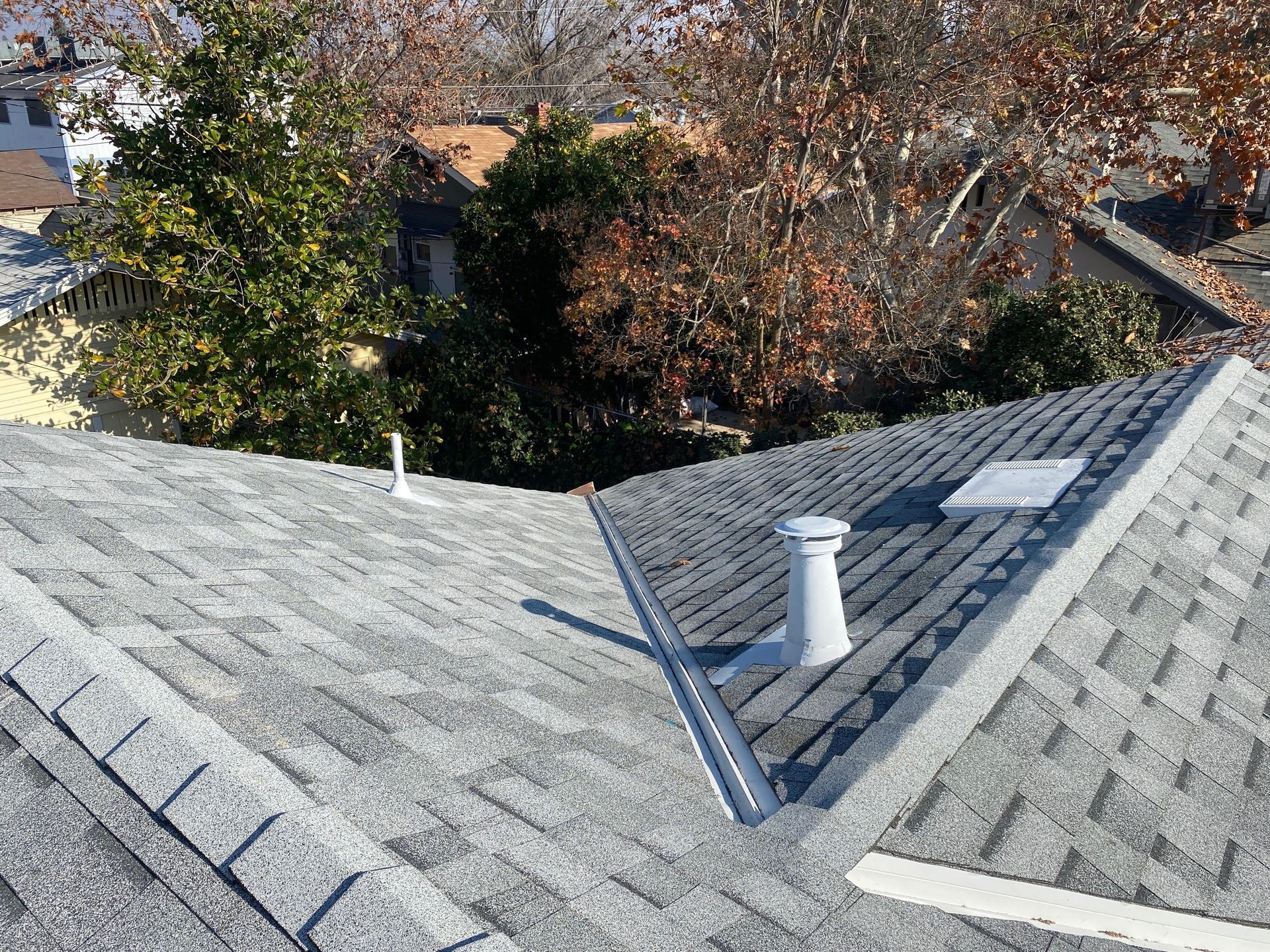 Gray shingled rooftops with a valley gutter and white vent pipe, viewed from above