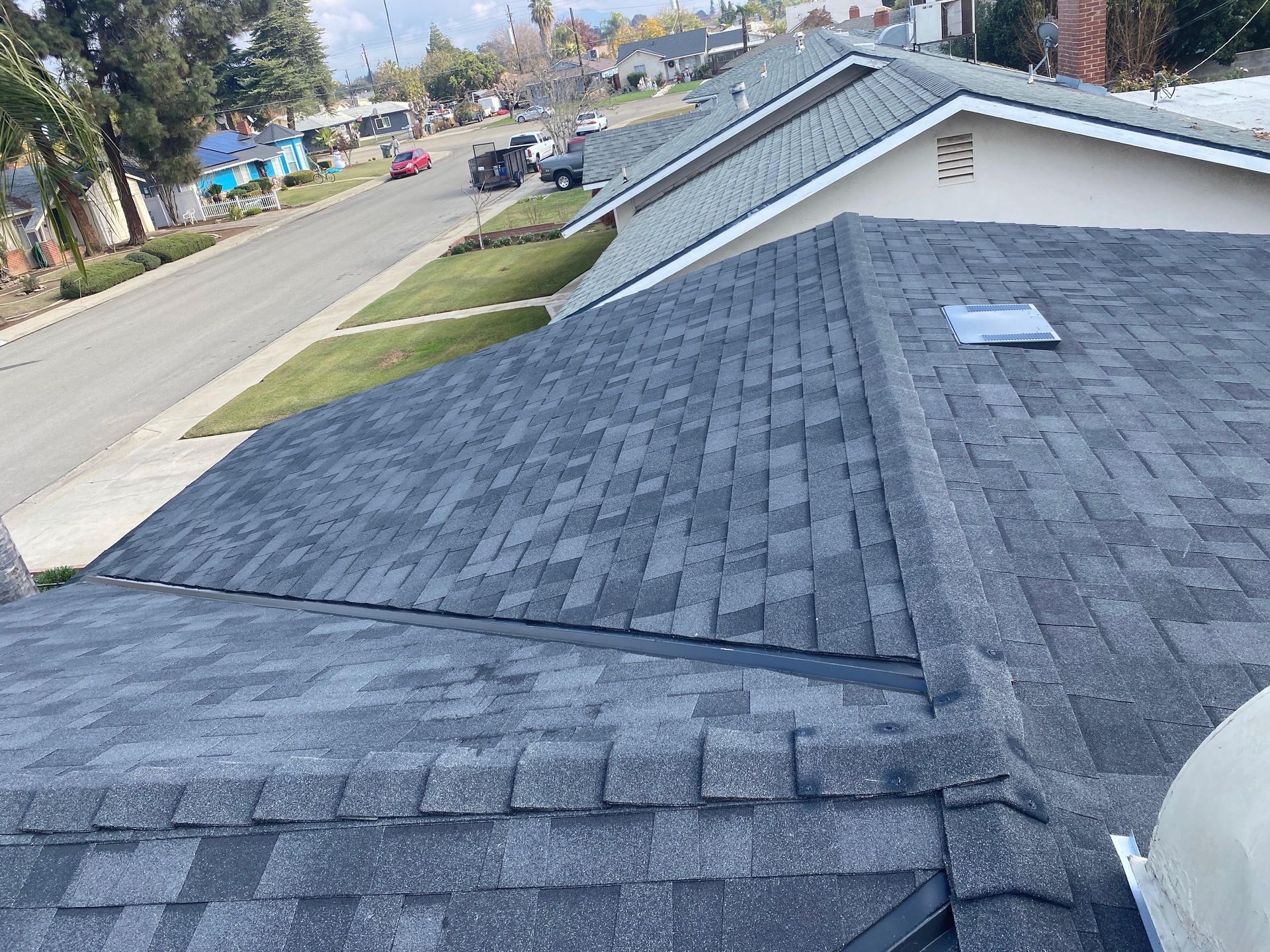 View from a shingled rooftop over a suburban street and neighboring houses on a clear day