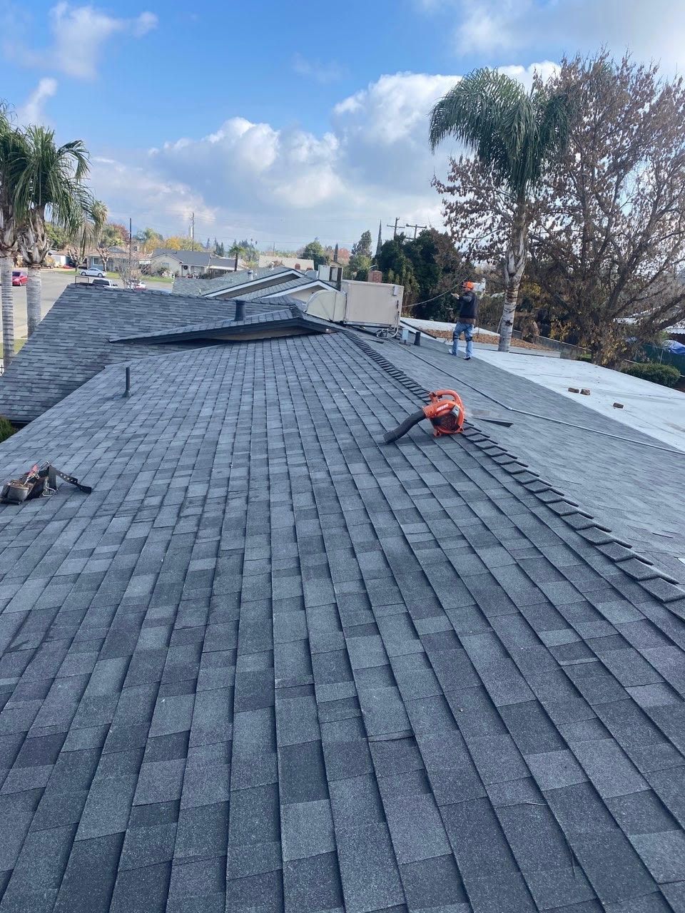 Roof under construction with gray shingles and a worker in an orange vest on a sloped roof