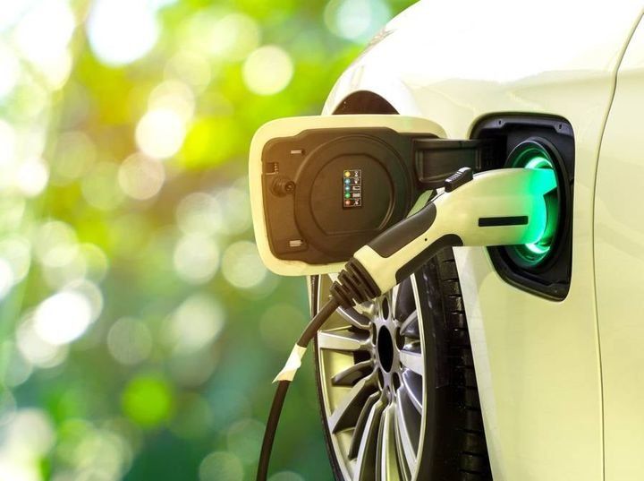 Voiture électrique en charge à une station équipée d'une prise de recharge verte connectée à la zone de la roue avant.
