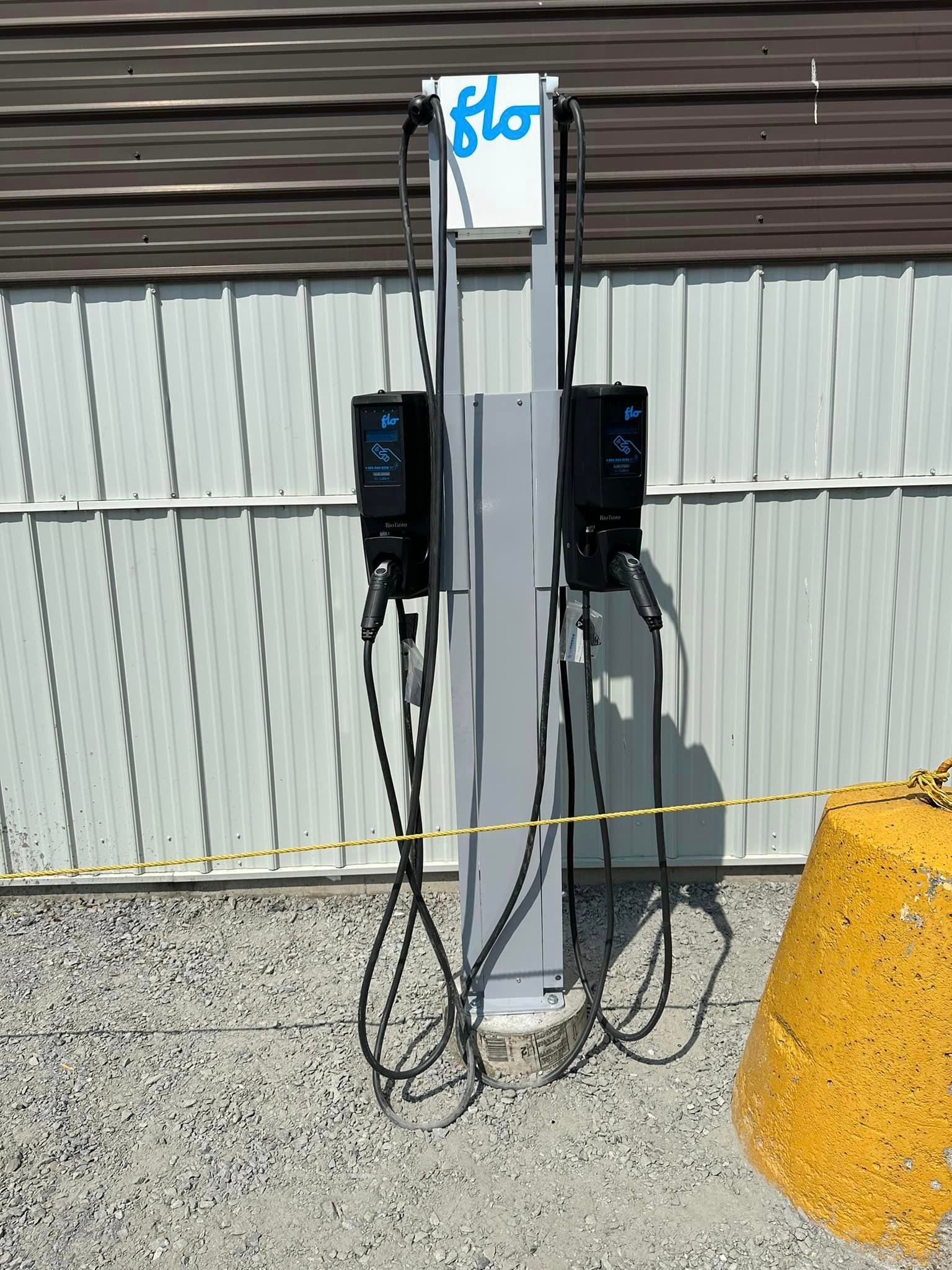 Station de recharge extérieure pour véhicules électriques avec deux chargeurs noirs montés sur un poteau gris à côté d'une clôture