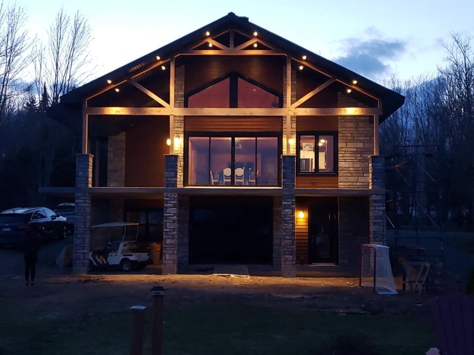 Vue de face d'une maison en bois éclairée au crépuscule, avec un garage et une toiture triangulaire.