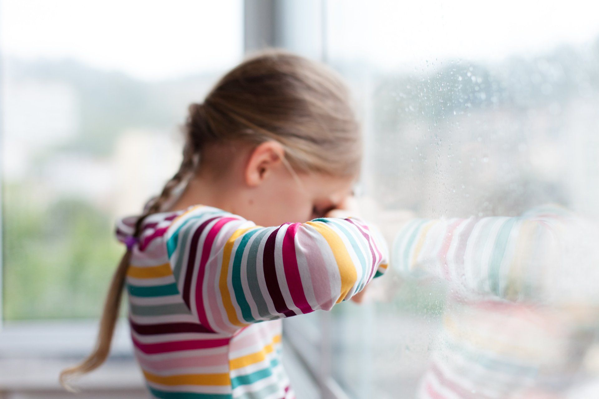 sad little girl with head against window