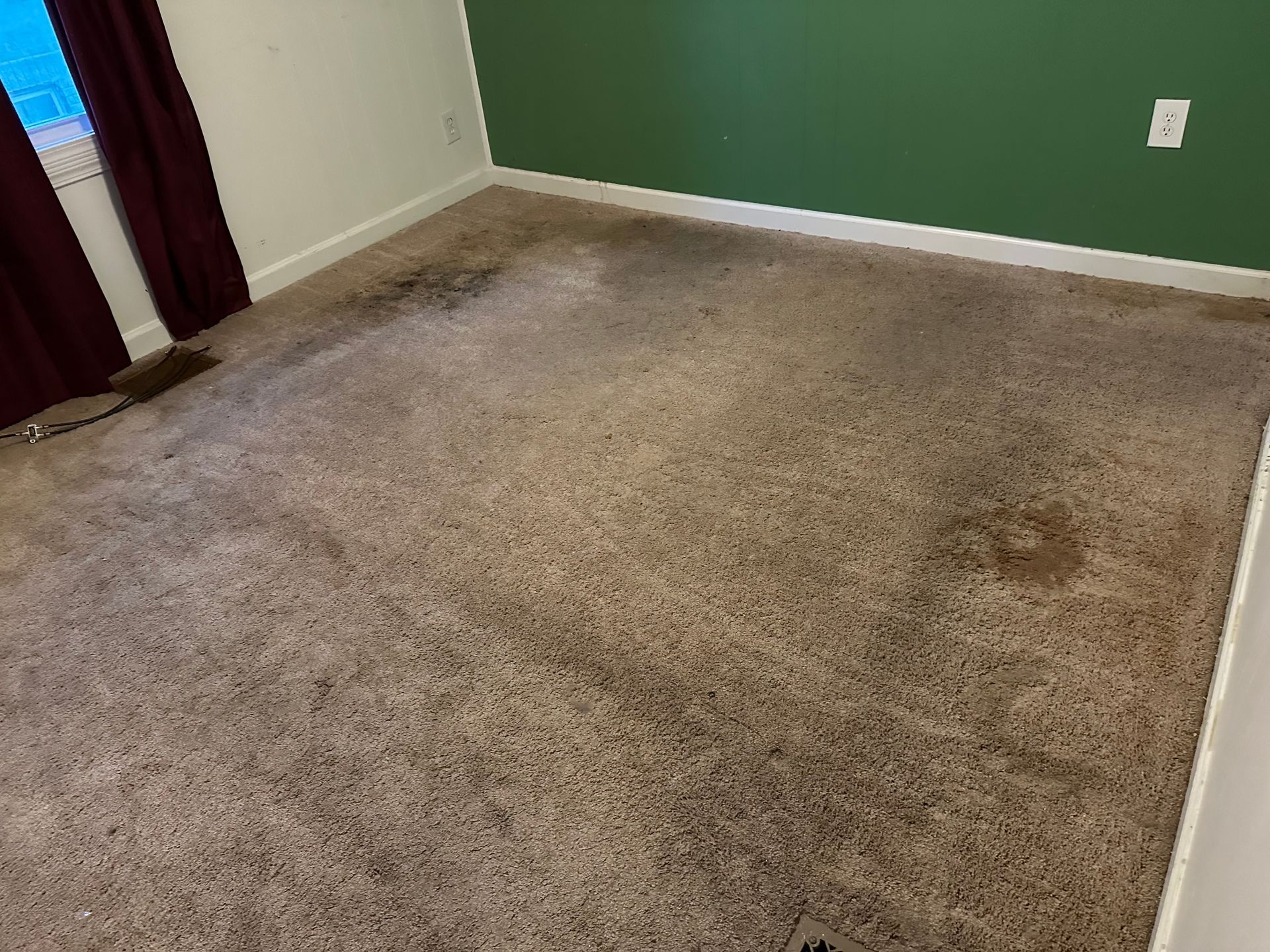 A room with a dirty carpet and a green wall.