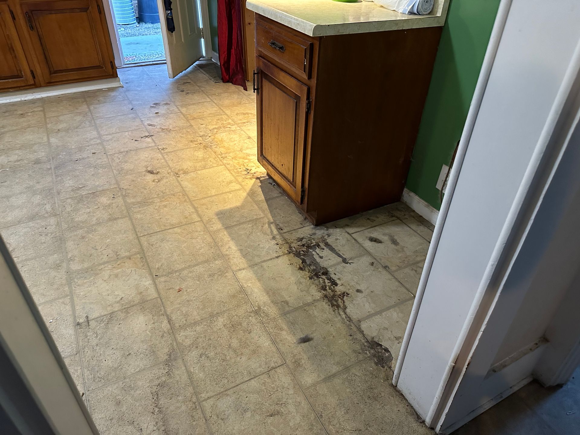 A kitchen with a dirty floor , cabinets , and a refrigerator.